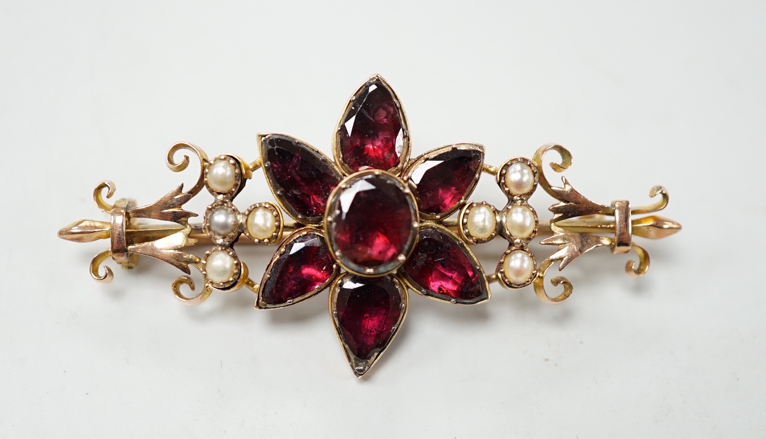 A late Victorian yellow metal, foil backed garnet and split pearl set flower head bar brooch, 55mm, gross weight 7.9 grams.